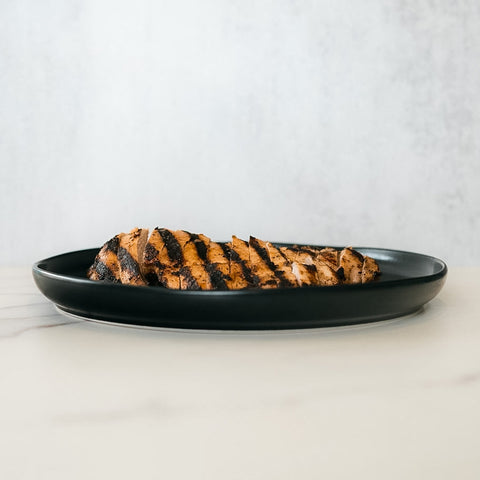 Competition Approved Grilled Chicken 1lb features sliced, halal chicken breast with visible char marks, arranged on a round black plate—ideal for meal prep and presented on a light surface with a neutral background.