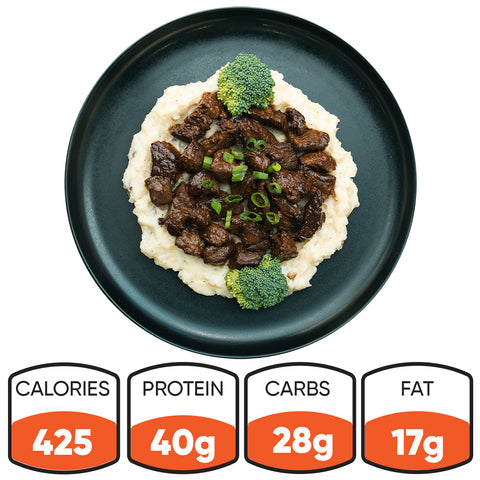 The Herb Butter Steak Tips Bowl features mashed potatoes topped with grass-fed steak tips, onions, green onions, and broccoli. This high-protein meal prep offers 425 calories, 40g protein, 28g carbs, and 17g fat.
