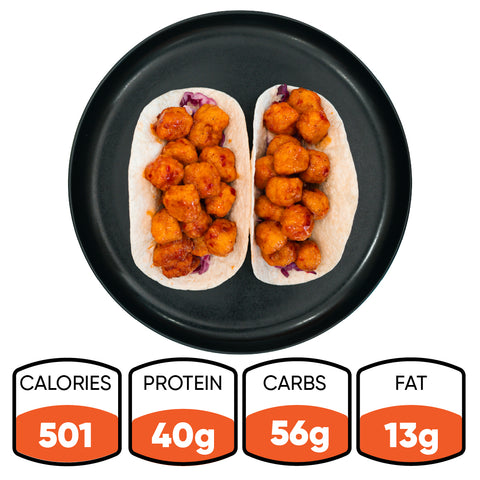 Two soft tacos filled with coated, sauced pieces on a black plate—these Honey Garlic Crispy Chicken Tacos are a delicious option for High-Protein Meal Prep. Nutritional info below: 501 calories, 40g protein, 56g carbs, 13g fat.