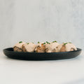 Keto Ricotta Meatballs—four meatballs with creamy sauce and fresh herbs on a black plate, set against a light background—make for a tasty, high-protein choice.