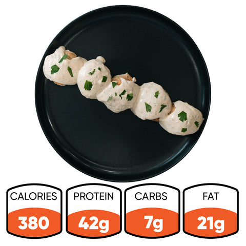 Five Keto Ricotta Meatballs topped with creamy white sauce and herbs are lined up on a black plate. Nutrition facts: 380 calories, 42g protein, 7g carbs, and 21g fat—making this a low-carb, high-protein dish.