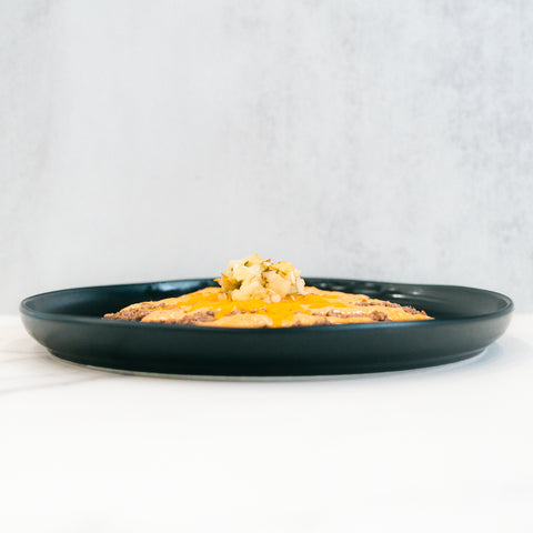A Low Carb Keto Cheeseburger Bowl served in a black plate features a high-protein, cheesy dish, topped with diced vegetables or garnish, set on a white surface with a light gray background.