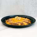 The Low Carb Keto Cheeseburger Bowl features ground beef topped with melted cheddar cheese in stripes and a center pile of diced pickles on a black plate—a high-protein, low-carb comfort dish against a minimalistic background.