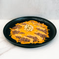 A black plate holds the Low Carb Keto Cheeseburger Bowl: cooked ground beef with melted cheddar, cheese sauce, and chopped onions—a tasty low-carb, high-protein meal.