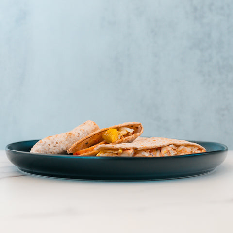A blue plate with two HFit Signature Folds—filled with cheese, yellow bell peppers, and grilled chicken—sits on a white surface against a light blue textured background, making it a perfect option for healthy meal prep.