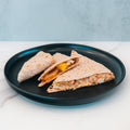 Three triangular pieces of the HFit Signature Fold—filled with vegetables, melted cheese, and seasoned grilled chicken—sit on a black plate against a light, marble-like background. Perfect for healthy meal prep or pairing with tangy ranch chipotle sauce.