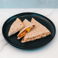 Three triangular HFit Signature Fold pieces with a whole wheat flatbread exterior and visible grilled chicken filling, arranged on a round black plate atop a white marble surface—a perfect option for healthy meal prep.