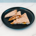 Three wedges of the Strongsville Chicken Ranch Fold, made with whole wheat tortillas and filled with HALAL Turkey bacon, cooked chicken, and vegetables, are arranged on a round black plate atop a white marble surface—a high-protein meal that’s as satisfying as it is visually appealing.