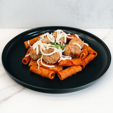 Rigatoni Meatballs: Rigatoni pasta with tomato sauce, four ground-beef meatballs, shredded cheese, and parsley on a black plate—a delicious macro-friendly meal prep option.