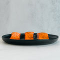 Three Competition Approved Lemon Pepper Salmon fillets 1lb are neatly arranged on a black plate, ideal for a low-carb, high-protein meal prep against a light, neutral background.