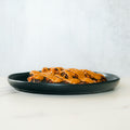 A black plate with Competition Approved Grilled Chicken W/ Smokin Poppie Sauce 1lb sits on a white surface against a light grey background—the ideal high-protein meal.