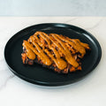 Competition Approved Grilled Chicken W/ Smokin Poppie Sauce 1lb is sliced and arranged on a black plate, topped with a thick, golden-brown sauce for a high-protein meal, served on a white marble surface.