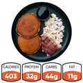 The Snickerdoodle Pancake Breakfast features high-protein pancakes, crumbled scrambled eggs, turkey bacon, and a cup of sugar-free syrup. Nutrition: 403 calories, 32g protein, 44g carbs, and 11g fat. Served on a black plate.