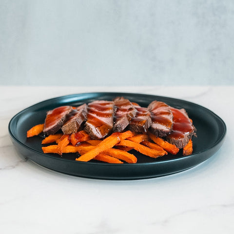 The Soho Steak Bowl offers sliced steak with savory sauce over sweet potato fries, served on a black plate—an Asian-inspired, healthy lunch perfect for any setting.