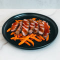 The Soho Steak Bowl features sliced steak with sauce over sweet potato fries, served on a black plate—a healthy, Asian-inspired lunch option presented on white marble.