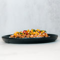 The Southwest Chicken Bowl features sliced grilled chicken, corn, diced red peppers, and herbs over white rice—a gluten-free meal prep option—served on a black plate with a light background.