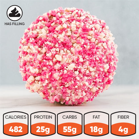A close-up of the Strawberry Crunch Milkshake Buffin Muffin reveals a round, pink and white snack ball with a crumbly texture and a delicious strawberry milkshake flavor. Nutrition facts display: 482 calories, 25g protein, 55g carbs, 18g fat, and 4g fiber—making it a high-protein treat. An icon highlights its filled center.