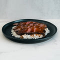 Teriyaki Flank Bowl: Tender sliced steak in teriyaki sauce over white rice, served on a dark plate atop white marble. An ideal option for healthy eating and quick meal prep.