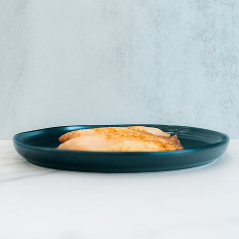 A teal plate with two pieces of Baked Herbed Tilapia 1lb Competition Approved sits on a white surface, perfect for meal prep or weight loss plans.