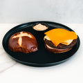 A black plate holds the Vegan Breakfast Sandwich, served open-faced with a plant-based patty, folded egg, cheddar cheese, and a creamy sauce on the side—ideal for those wanting a high-protein breakfast.