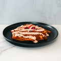 The Nacho Average Vegan Bowl features plant-based protein, creamy sauce, and tortilla strips atop a savory waffle, all served meatless on a black plate against a light backdrop.