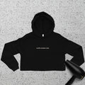 A black cropped hoodie with the text buffin baddie club in small white letters on the chest, laid flat on a speckled surface next to a black hair dryer.