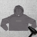 A gray cropped hoodie with the words buffin baddie club printed on the front lies on a speckled surface. A black hair dryer is partially visible in the lower right corner.